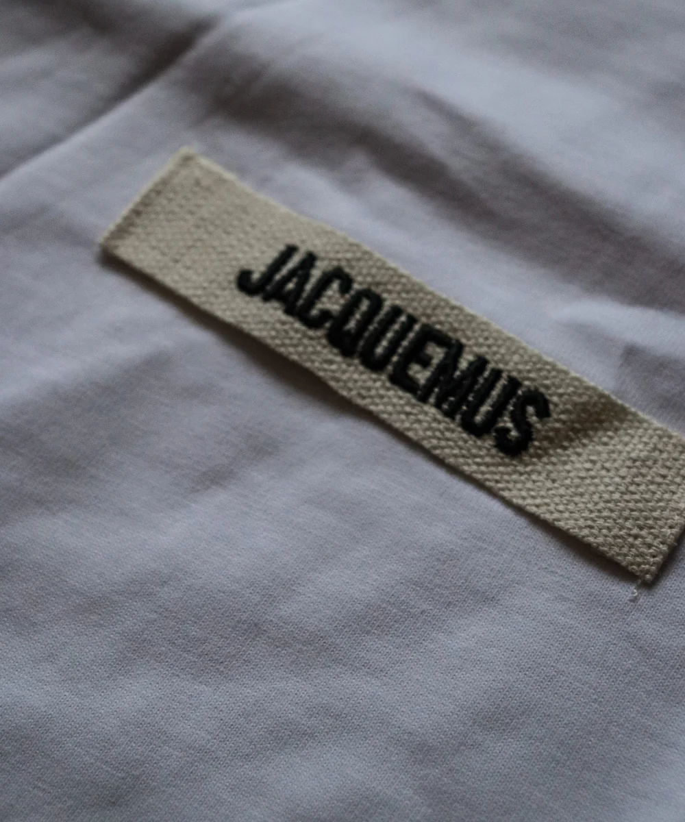 White shirt — Jacquemus-labelled chest badge close-up